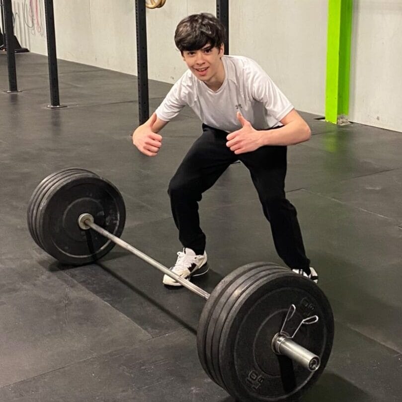male teen giving thumbs up standing near barbell
