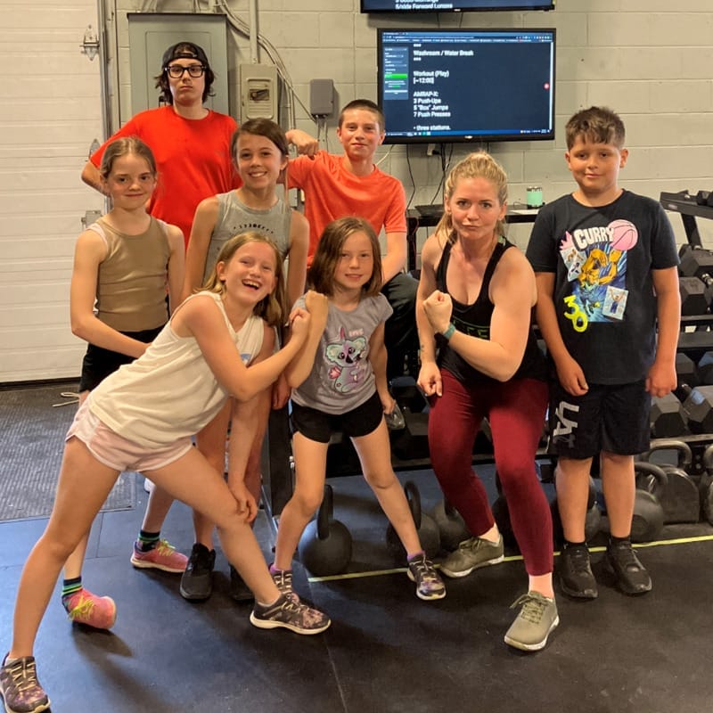 female crossfit coach and group of young children flexing muscles