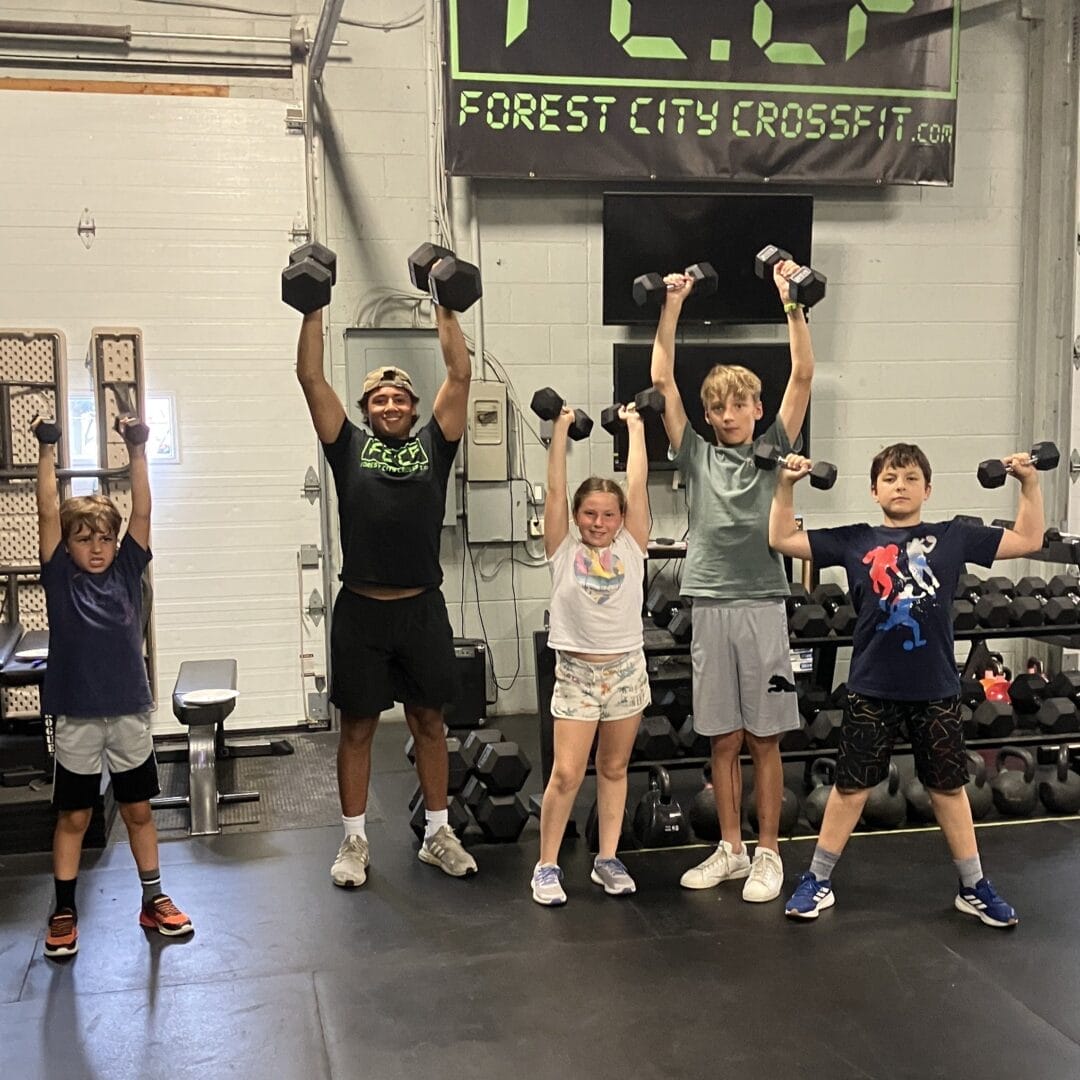 young male coach and child members holding up dumbbells