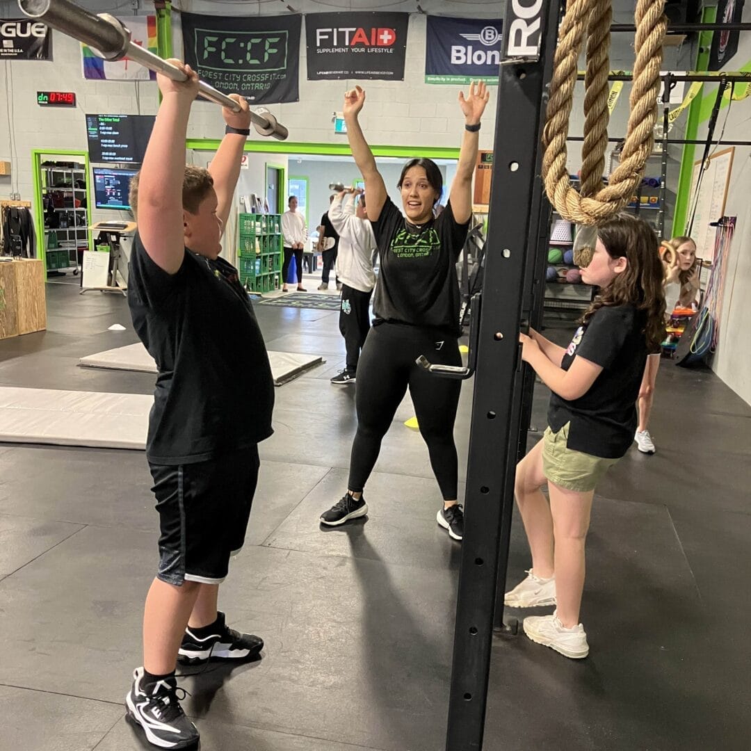 female coaching demonstrating shoulder press to a young boy while a girl watches
